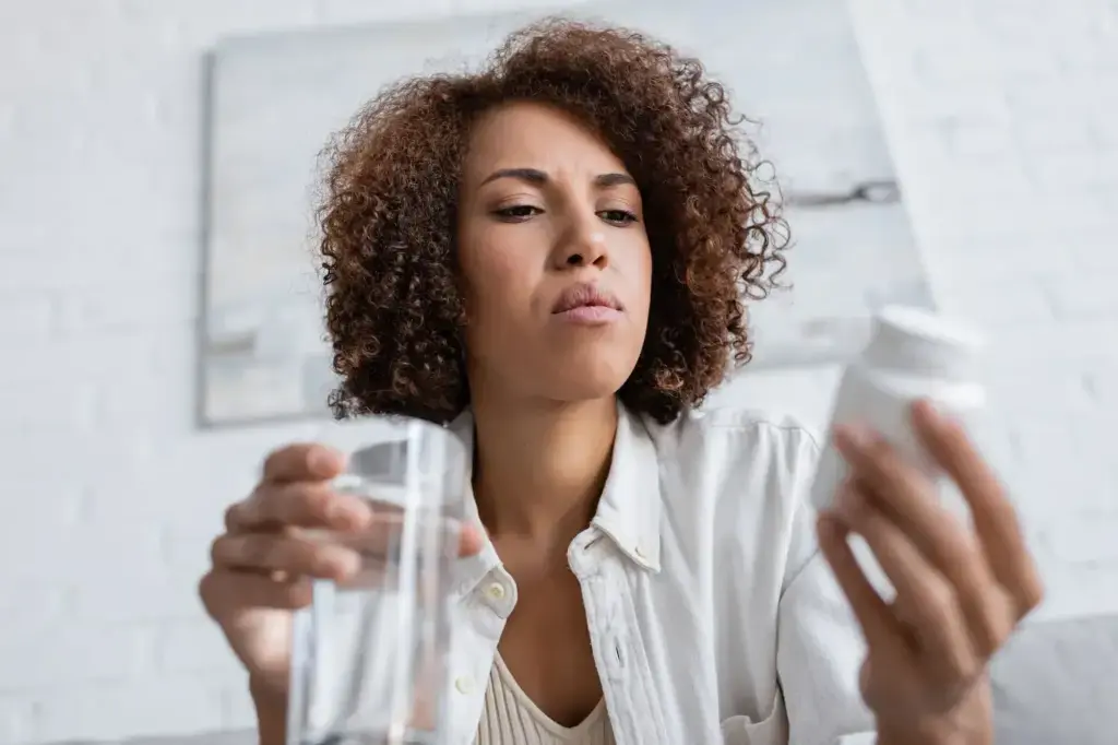 Woman examining a pill bottle while holding a glass of water