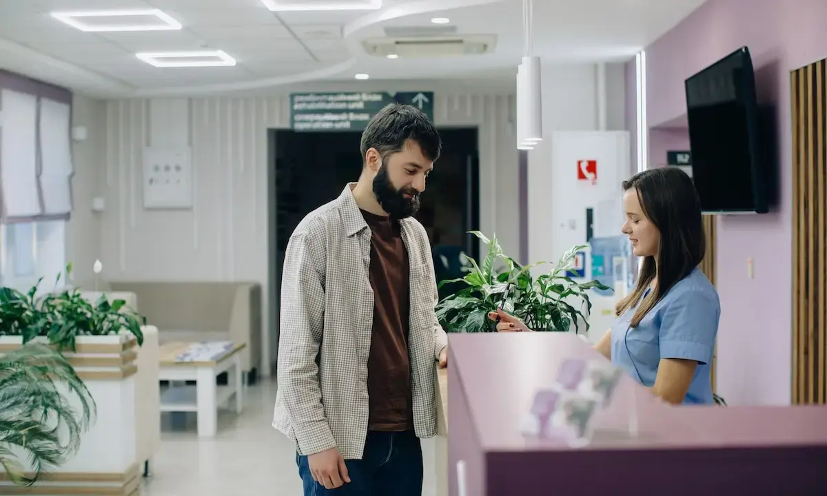 Man checking in at clinic reception with smiling receptionist