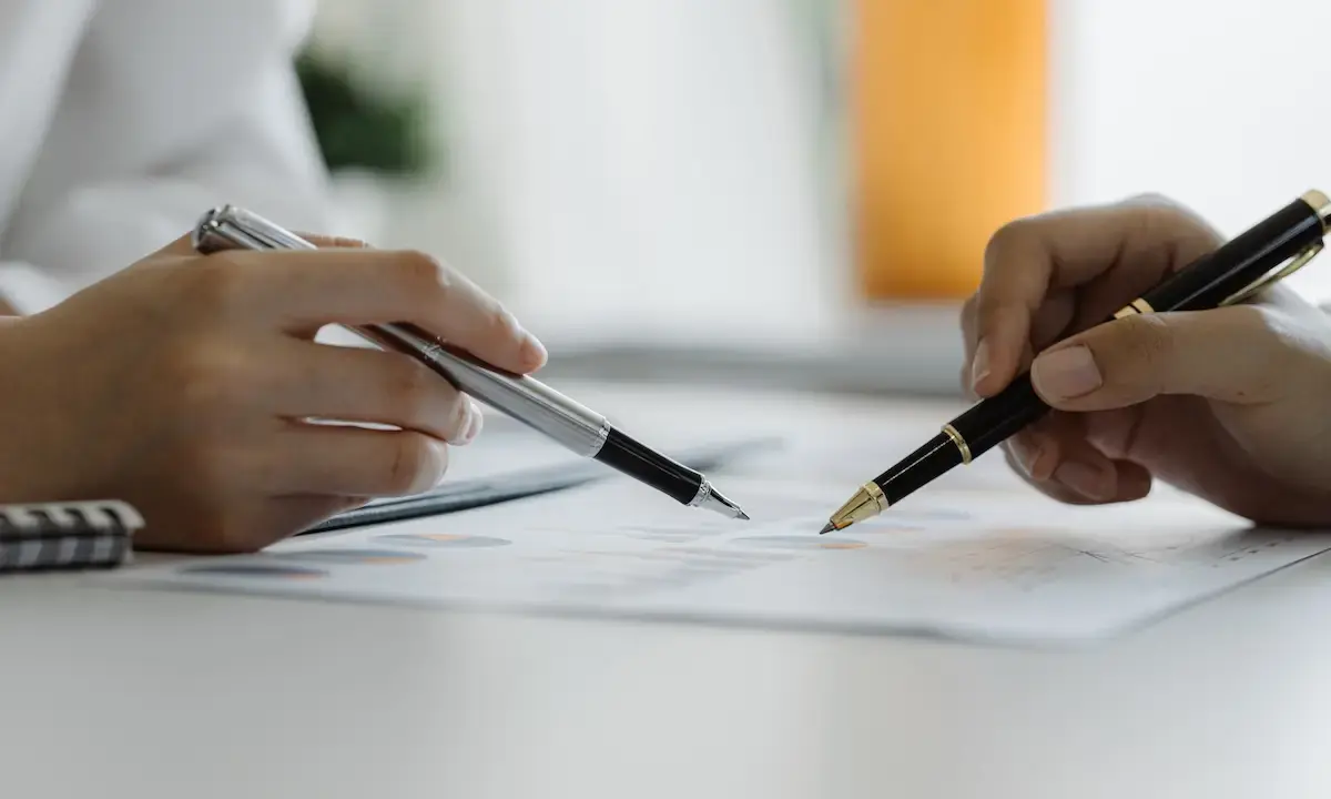 Two people pointing pens at documents during a paperwork discussion