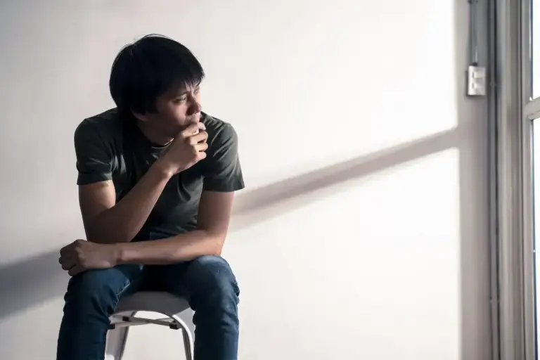 man seated on a stool gazing pensively toward a window