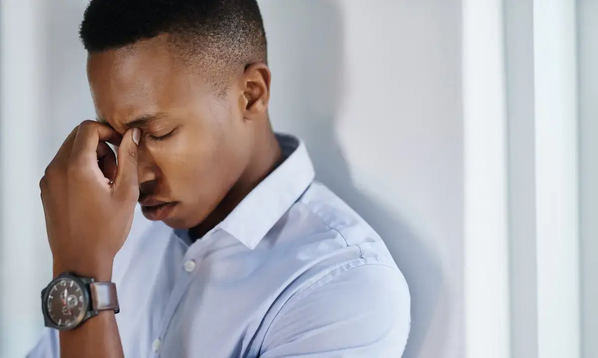 Young man pinching bridge of nose, appearing stressed and tired
