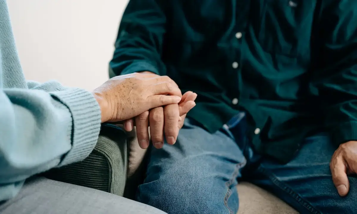 Older adult's hand gently held by another person on a couch