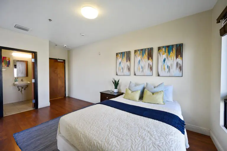 Sunny, comfortable recovery residence bedroom with bed and en-suite bathroom