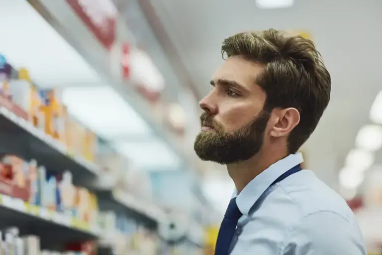 Man considering medication options at pharmacy shelves