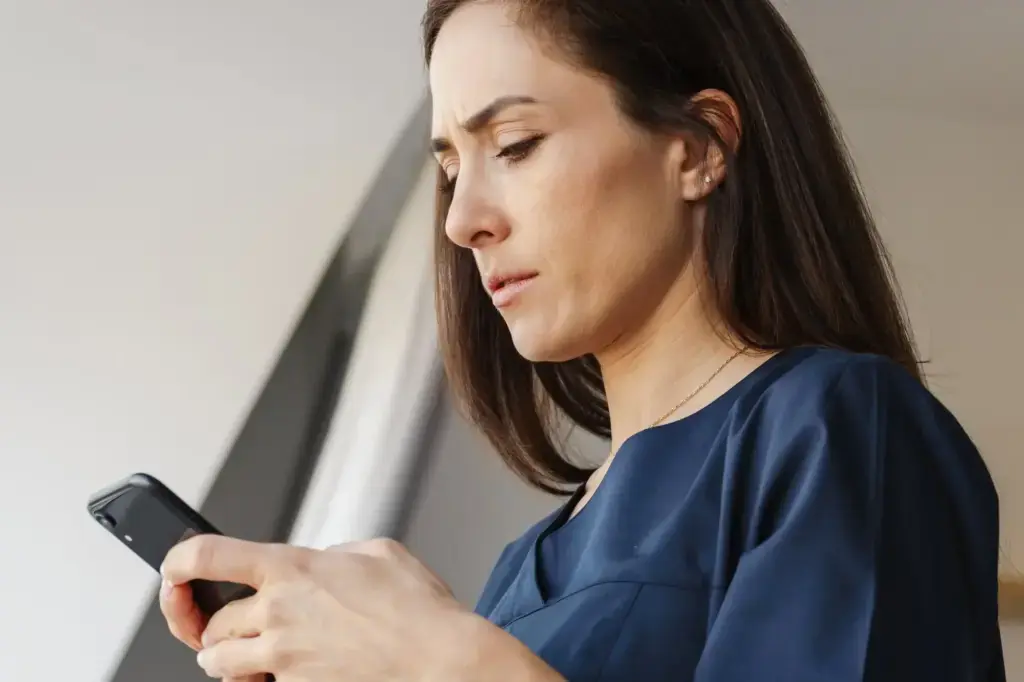 Woman reading smartphone with concerned expression near window