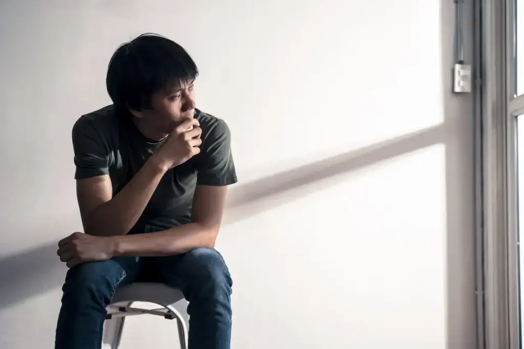man seated on a stool gazing pensively toward a window